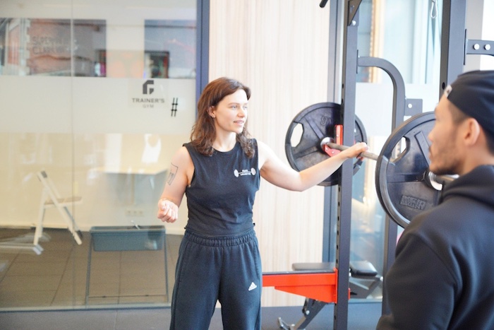 Lena Traninger im Gespräch mit einem Klienten an der Langhantel im Trainer's Gym in der Margaretenstraße 87, 1050 Wien